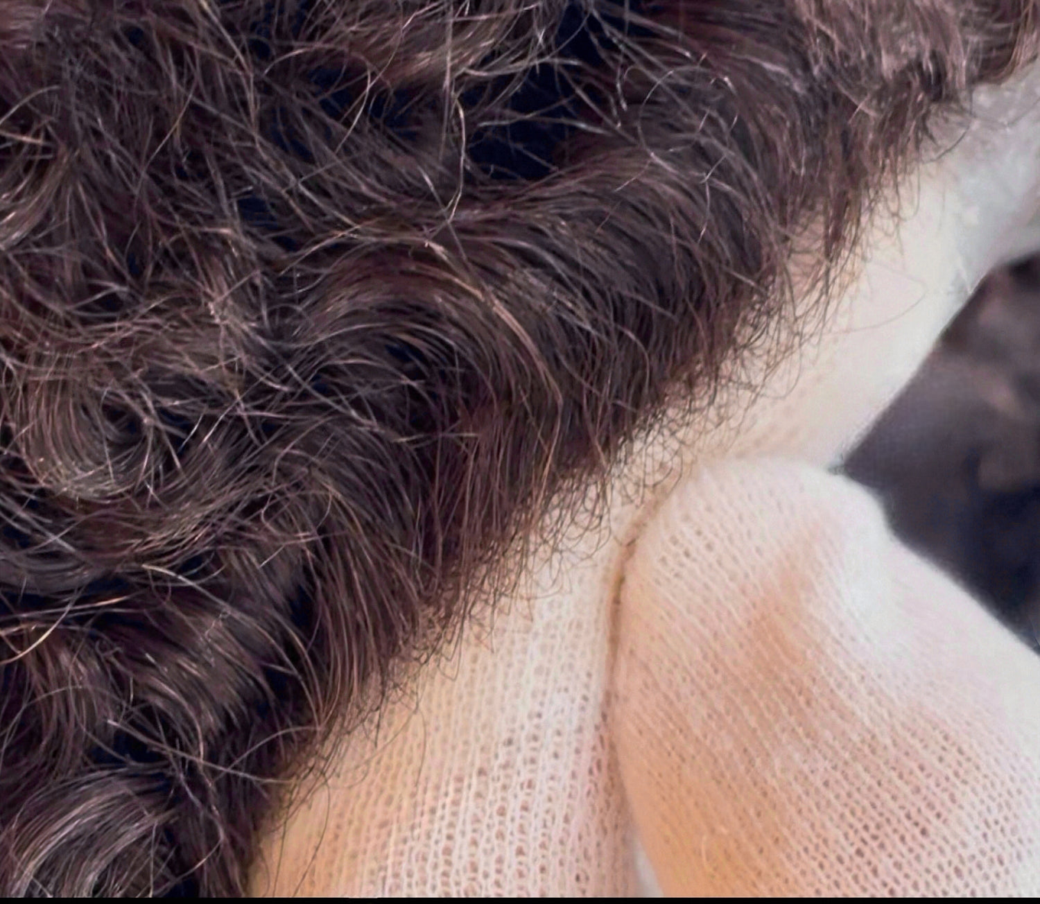 Close-up of a curly hairpiece for men, held with gloves at the hairline, showing a natural invisible front hairline effect.